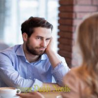 5 virhettä, jotka sugar baby tekee ensimmäisillä treffeillä. Mies tylsistyneellä ilmeellä nojaa päätään käteensä, vaikuttaen olevan tylsällä treffeillä naisen kanssa.