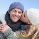 Nainen suutelee kypsää miestä, joka käyttää hattua, molemmat hymyilevät ja ovat onnellisia.